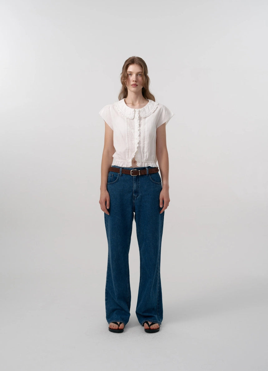 The Daina Ruffle Collar Blouse features a delicate lace trim along the hem, adding a refined and expert touch to its design. Crafted from a soft, ivory cotton fabric, this blouse combines sophisticated details such as a ruffled collar and precise stitching to ensure both elegance and durability. Ideal for those who appreciate meticulous craftsmanship and understated femininity.