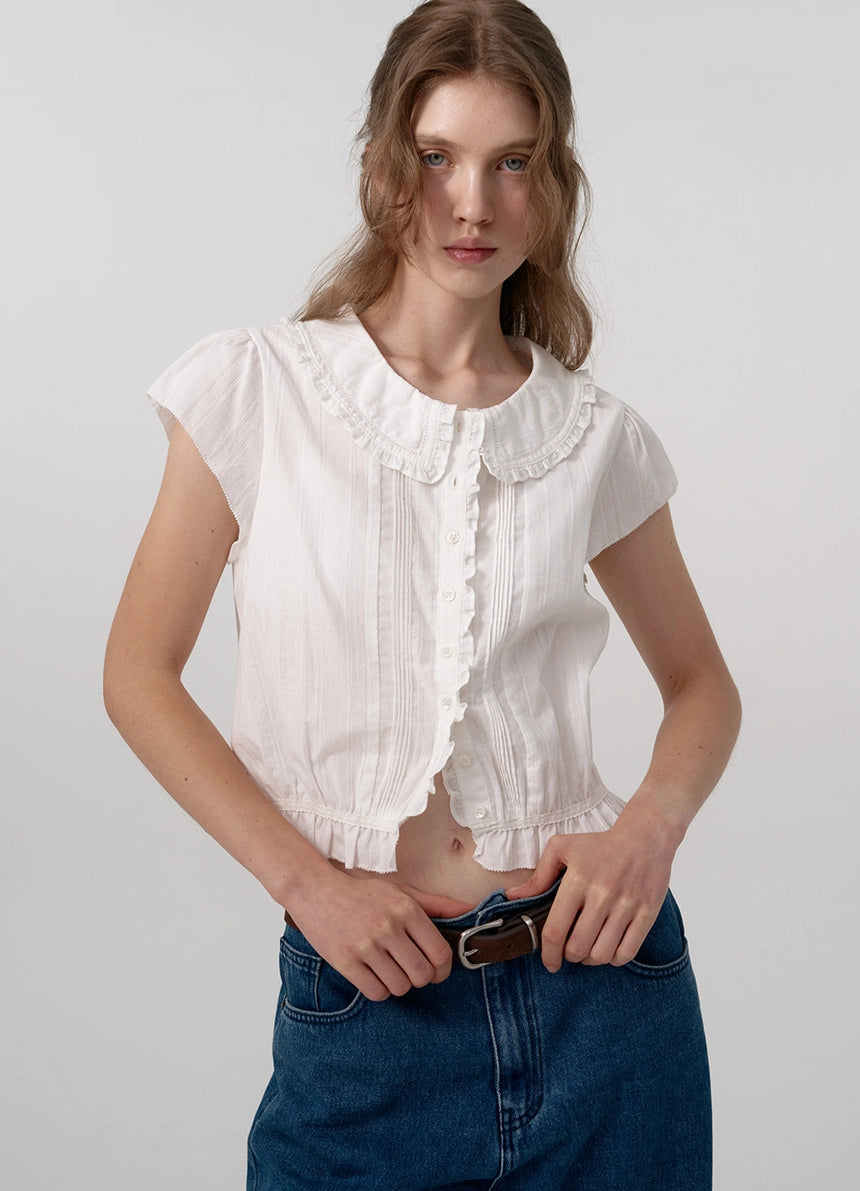 The Daina Ruffle Collar Blouse features a delicate lace trim along the hem, adding a refined and expert touch to its design. Crafted from a soft, ivory cotton fabric, this blouse combines sophisticated details such as a ruffled collar and precise stitching to ensure both elegance and durability. Ideal for those who appreciate meticulous craftsmanship and understated femininity.
