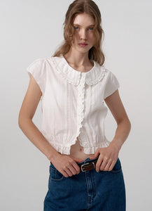 The Daina Ruffle Collar Blouse features a delicate lace trim along the hem, adding a refined and expert touch to its design. Crafted from a soft, ivory cotton fabric, this blouse combines sophisticated details such as a ruffled collar and precise stitching to ensure both elegance and durability. Ideal for those who appreciate meticulous craftsmanship and understated femininity.