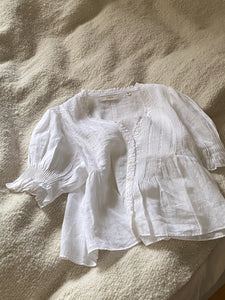 The Karlie Top by Doen combines lightweight ramie fabric with carefully designed details to create a refined, vintage-inspired piece. Its plunging V-neckline with soft ruffles and precise pintuck accents evoke Edwardian elegance. A starburst button line adds subtle sophistication, while short puffed sleeves introduce a modern, playful touch. Whether worn loose or tucked into high-waisted jeans, this top elevates your wardrobe with timeless style and effortless grace.