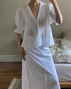 The Karlie Top by Doen combines lightweight ramie fabric with carefully designed details to create a refined, vintage-inspired piece. Its plunging V-neckline with soft ruffles and precise pintuck accents evoke Edwardian elegance. A starburst button line adds subtle sophistication, while short puffed sleeves introduce a modern, playful touch. Whether worn loose or tucked into high-waisted jeans, this top elevates your wardrobe with timeless style and effortless grace.