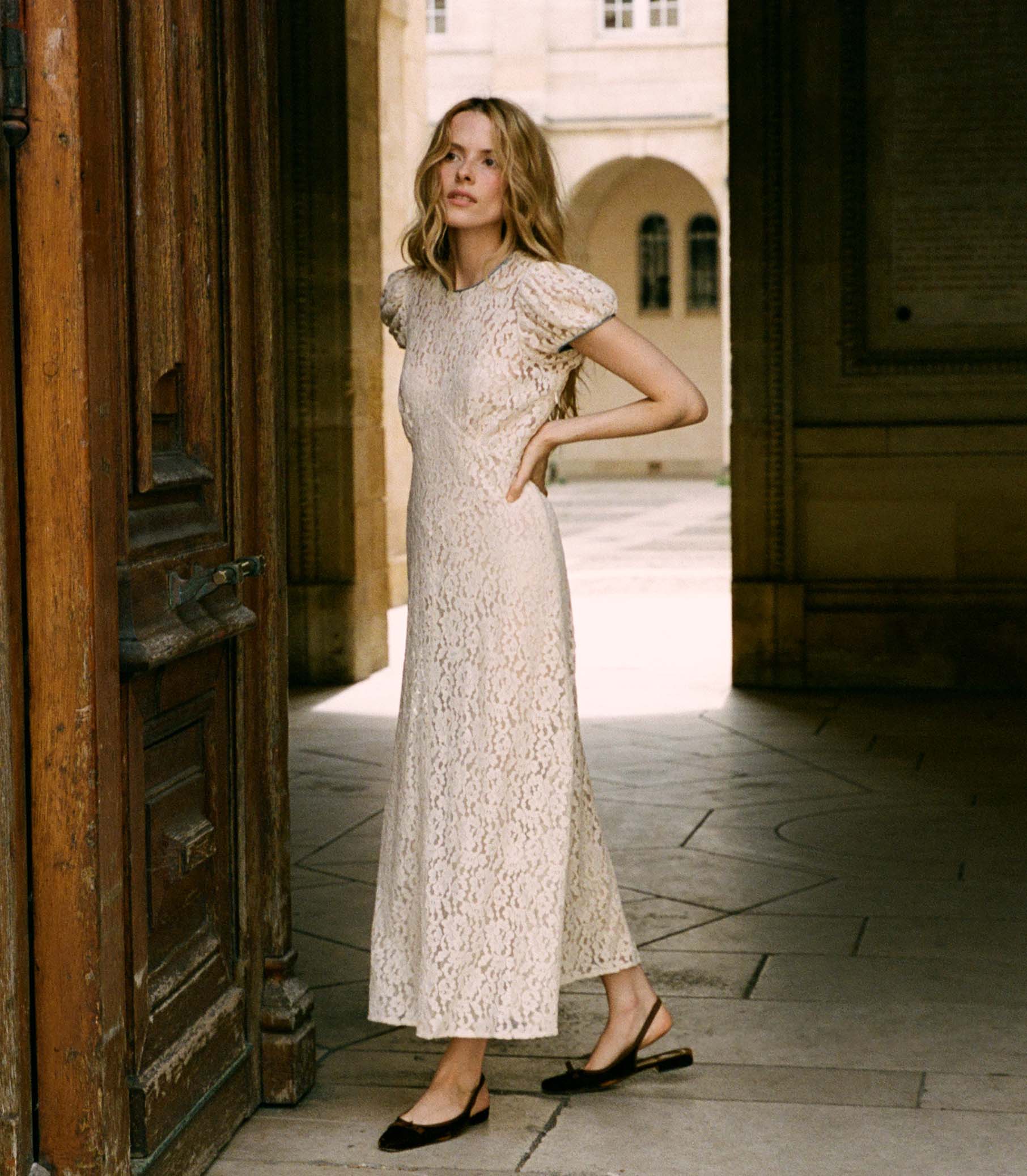 The Katarina Dress by Doen features a refined silhouette crafted from delicate corded lace, enhanced with satin trims along the neckline and puffed sleeves. Designed with a full lining, it offers both elegance and assured coverage, making it a sophisticated choice for special occasions.