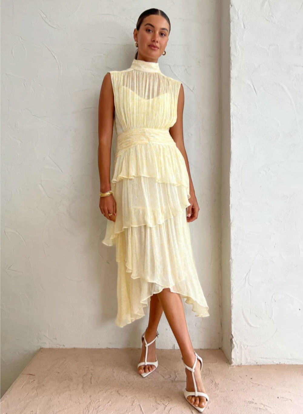 Introducing the Gina Sleeveless Ruched Midi Dress in Limoncello - a must-have for any special occasion. Crafted from semi-sheer chiffon, this dress boasts a high neck and adjustable rouleau straps for a perfect fit. With its fitted waist and asymmetrical tiered skirt, this dress exudes elegance and style. Perfect for formal events and celebrations.