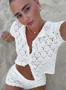 The Blossom Crochet Set features a button-up top with a round neckline and cap sleeves, paired with micro shorts offering a low-rise fit and elasticated waistband for comfort. Crafted from non-stretch mesh material without lining or pockets, this set emphasizes breathability and a lightweight feel, perfect for layering or warm weather wear. Its delicate crocheted design presents a sophisticated yet relaxed aesthetic ideal for curated vintage-inspired wardrobes.