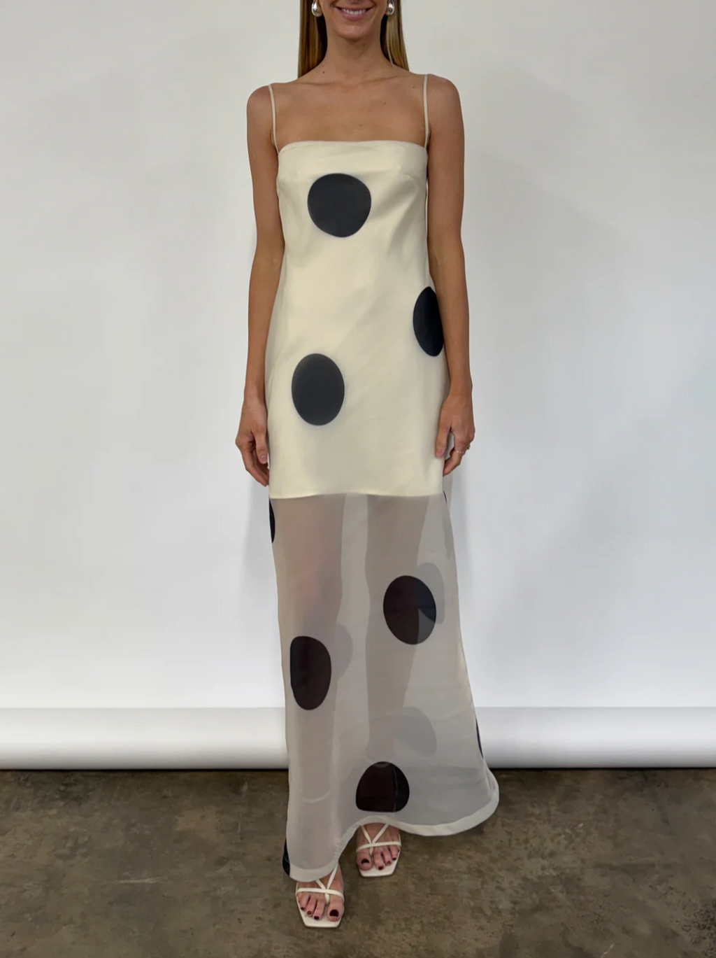 The Mila Maxi Dress in Ivory Polka by Nicole features sheer organza adorned with striking polka dots, shaping a sleek column silhouette. Its half-lined design and elasticated back ensure comfort and adaptability, while the option to wear it with or without straps provides versatile styling choices perfect for refined occasions.