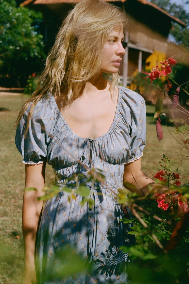 The Brynne Dress in the seasonal Pansy Blues print by Christy Dawn combines delicate femininity with adjustable comfort. It features a low scoop neckline complemented by a drawstring tie at both the neck and waist, allowing a custom fit that enhances your silhouette. Elasticated seams ensure ease of movement, making this dress as practical as it is stylish for versatile wear throughout the season.