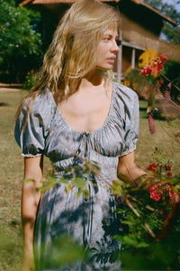 The Brynne Dress in the seasonal Pansy Blues print by Christy Dawn combines delicate femininity with adjustable comfort. It features a low scoop neckline complemented by a drawstring tie at both the neck and waist, allowing a custom fit that enhances your silhouette. Elasticated seams ensure ease of movement, making this dress as practical as it is stylish for versatile wear throughout the season.