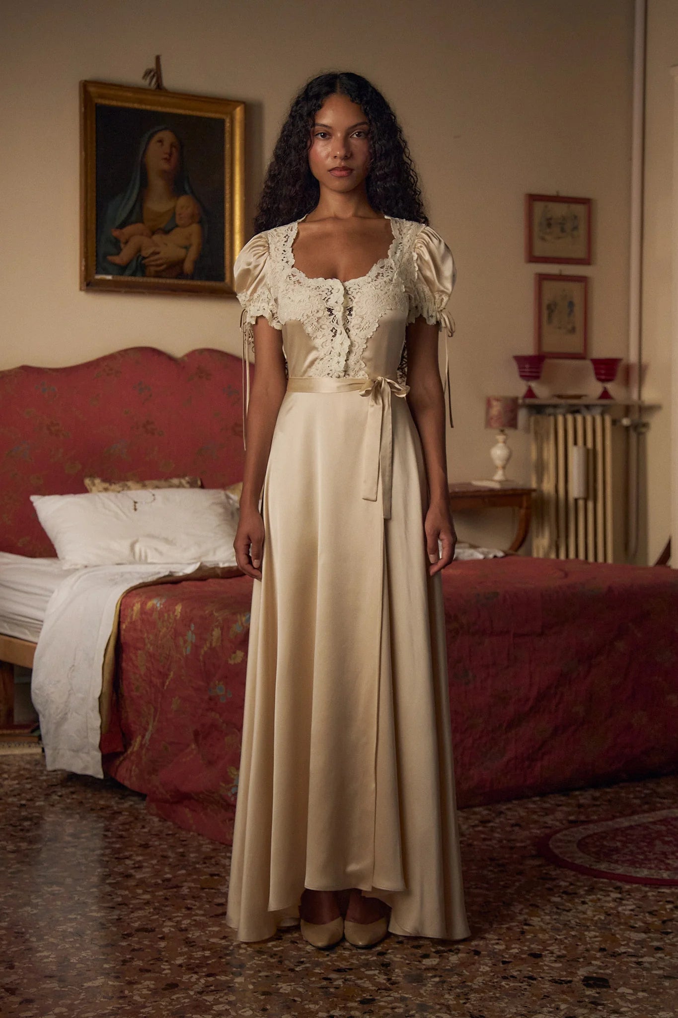 Crafted from luxurious silk charmeuse, the Unwrap Me Gown in Crème features delicate lace trim along the neckline and sleeves, enhancing its refined silhouette. Lace-covered buttons with hidden snaps offer elegant closure at the center front, while a matching silk charmeuse belt with chain stitch loops and snaps defines the waist. An adjustable slit secured by hook and thread loops adds both comfort and sophistication, making this gown a masterful blend of exquisite detail and expert tailoring.
