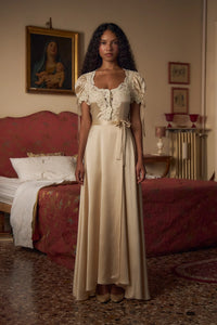 Crafted from luxurious silk charmeuse, the Unwrap Me Gown in Crème features delicate lace trim along the neckline and sleeves, enhancing its refined silhouette. Lace-covered buttons with hidden snaps offer elegant closure at the center front, while a matching silk charmeuse belt with chain stitch loops and snaps defines the waist. An adjustable slit secured by hook and thread loops adds both comfort and sophistication, making this gown a masterful blend of exquisite detail and expert tailoring.
