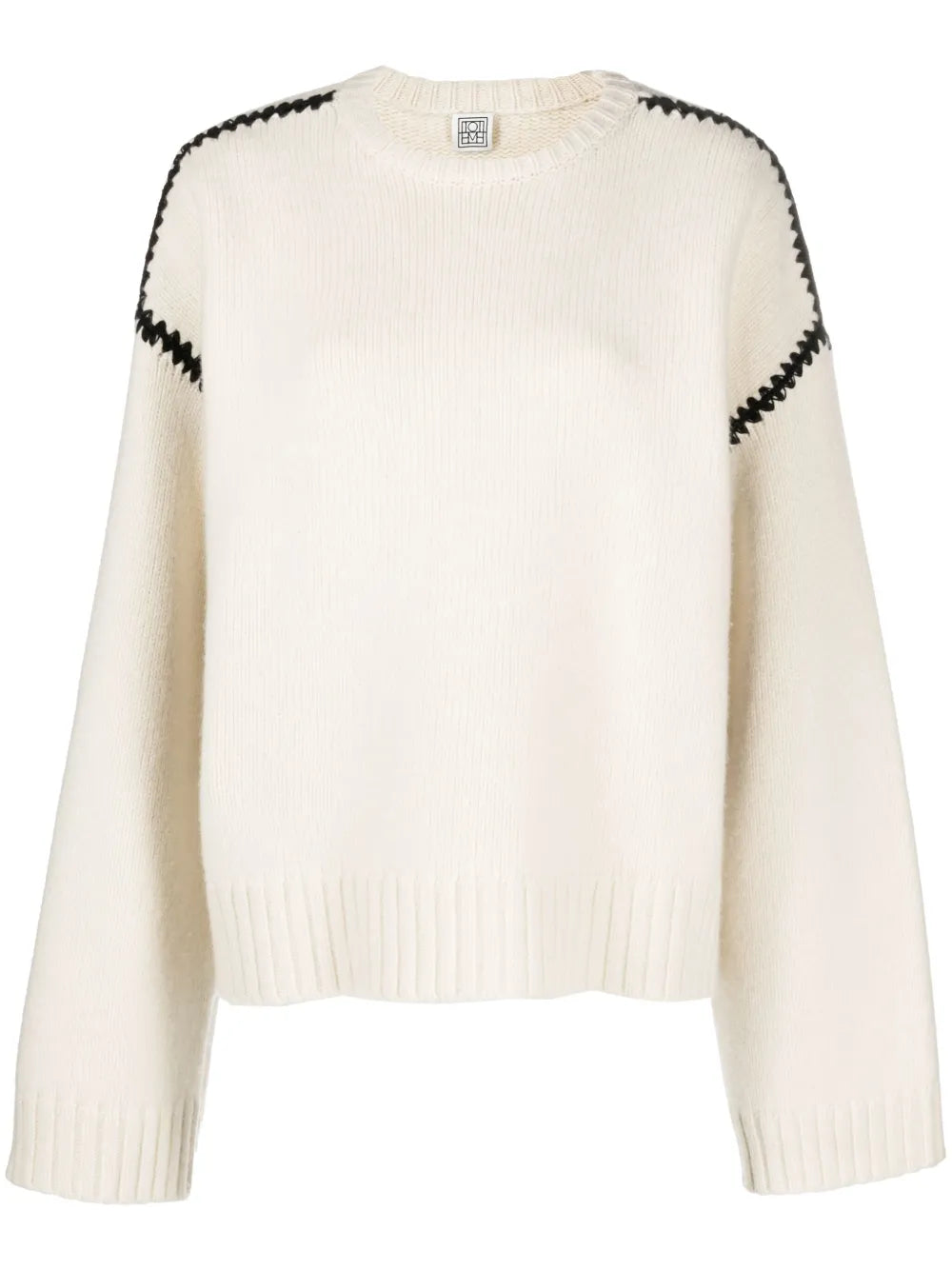This TOTEME wool jumper exemplifies contemporary minimalism with refined craftsmanship. Constructed from pure wool in a pristine cream-white, it features distinctive black whipstitch detailing that adds subtle visual interest without compromising the brand's signature understated aesthetic. The relaxed silhouette includes drop shoulders and generously proportioned long sleeves, while ribbed cuffs and hem provide structure and definition. 