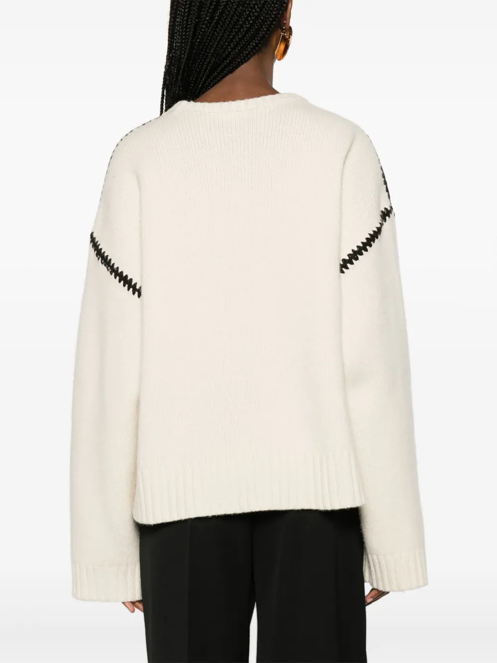 This TOTEME wool jumper exemplifies contemporary minimalism with refined craftsmanship. Constructed from pure wool in a pristine cream-white, it features distinctive black whipstitch detailing that adds subtle visual interest without compromising the brand's signature understated aesthetic. The relaxed silhouette includes drop shoulders and generously proportioned long sleeves, while ribbed cuffs and hem provide structure and definition. 
