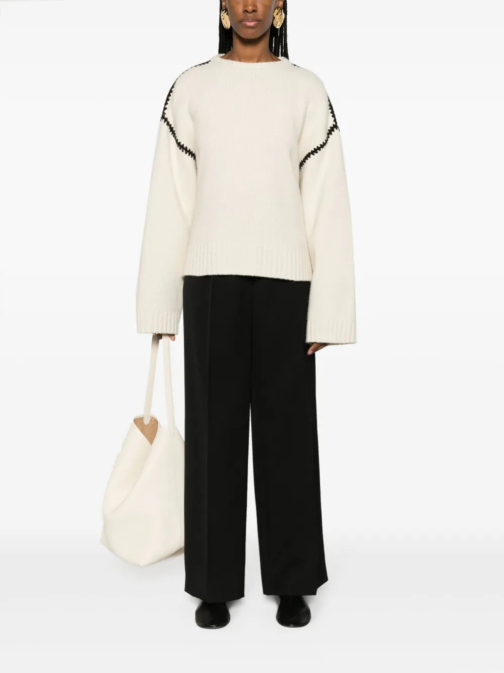 This TOTEME wool jumper exemplifies contemporary minimalism with refined craftsmanship. Constructed from pure wool in a pristine cream-white, it features distinctive black whipstitch detailing that adds subtle visual interest without compromising the brand's signature understated aesthetic. The relaxed silhouette includes drop shoulders and generously proportioned long sleeves, while ribbed cuffs and hem provide structure and definition. 