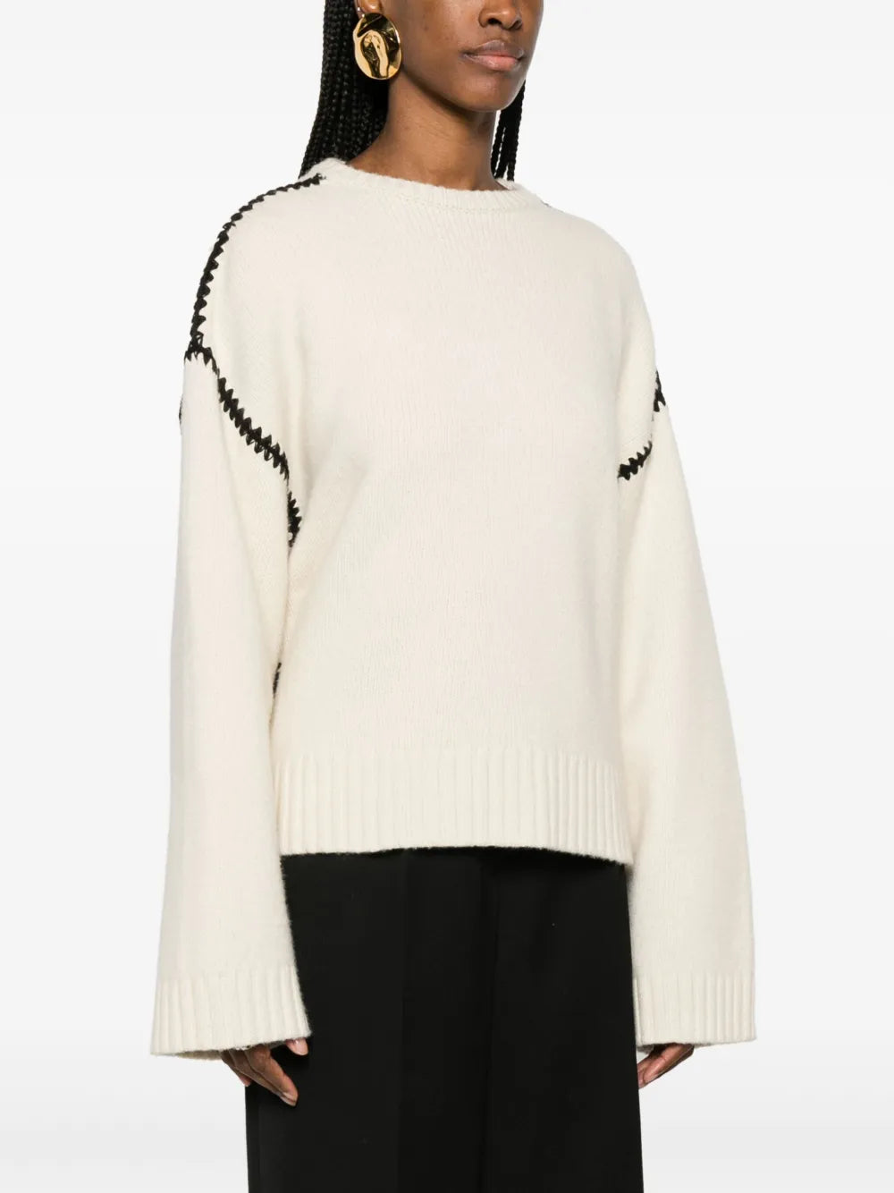 This TOTEME wool jumper exemplifies contemporary minimalism with refined craftsmanship. Constructed from pure wool in a pristine cream-white, it features distinctive black whipstitch detailing that adds subtle visual interest without compromising the brand's signature understated aesthetic. The relaxed silhouette includes drop shoulders and generously proportioned long sleeves, while ribbed cuffs and hem provide structure and definition. 