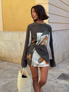 The Constance Twist Mini Dress is made from delicate silk crepe adorned with artistic floral prints and bold borders. This dress offers a relaxed silhouette, showcasing long sleeves with gentle flares and a distinctive contrasting overlay accented by a twisted detail at the waist.
