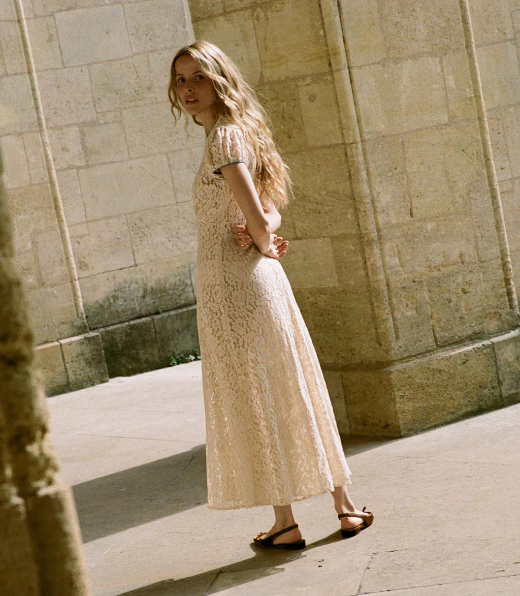 The Katarina Dress by Doen features a refined silhouette crafted from delicate corded lace, enhanced with satin trims along the neckline and puffed sleeves. Designed with a full lining, it offers both elegance and assured coverage, making it a sophisticated choice for special occasions.