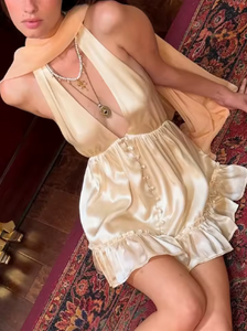 The Caroline Dress by Fait par Foutch is crafted from medium-weight 100% silk charmeuse, offering a luxurious, smooth texture that drapes elegantly. Fully lined with pure silk for enhanced comfort, it features functional silk-covered buttons and loops down the center front. Its low V-neckline and halter straps tie into an adjustable bow at the neck, providing a customizable fit. The low back design includes hidden elastic at the waist, ensuring a flattering silhouette and secure fit. 
