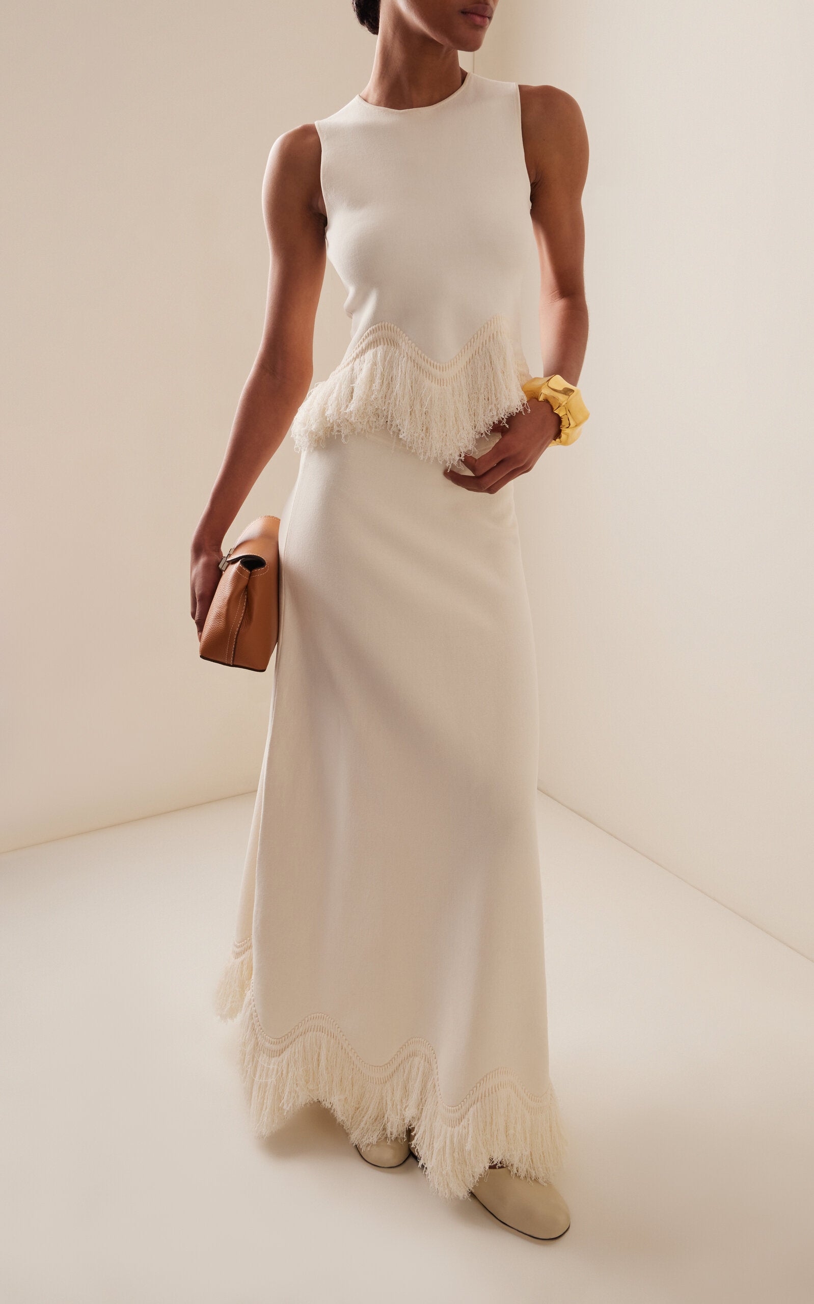 The 'Paulina' skirt offers a graceful A-line shape that gently widens toward its distinctive zig-zag fringe-trimmed hem. Complete the look by pairing it with the coordinating 'Koa' top, which boasts a sleek, sleeveless design accented by a matching zig-zag fringe detail at the hem.