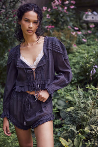 Experience timeless elegance with the Florence Set in Black, designed for both comfort and style. The structured bed jacket features front tie closures, delicate pleated piecing, and banded trumpet sleeves accented by intricate embroidery and ruffle trim. Coordinating shorts offer a drawstring waist for a customizable fit, complemented by ruffle details, pleated patterns, and embroidered accents with a graceful curved hem. Perfect for lounging with refined sophistication.