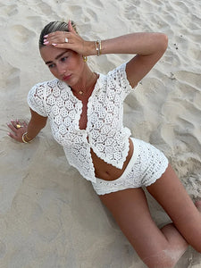 The Blossom Crochet Set features a button-up top with a round neckline and cap sleeves, paired with micro shorts offering a low-rise fit and elasticated waistband for comfort. Crafted from non-stretch mesh material without lining or pockets, this set emphasizes breathability and a lightweight feel, perfect for layering or warm weather wear. Its delicate crocheted design presents a sophisticated yet relaxed aesthetic ideal for curated vintage-inspired wardrobes.