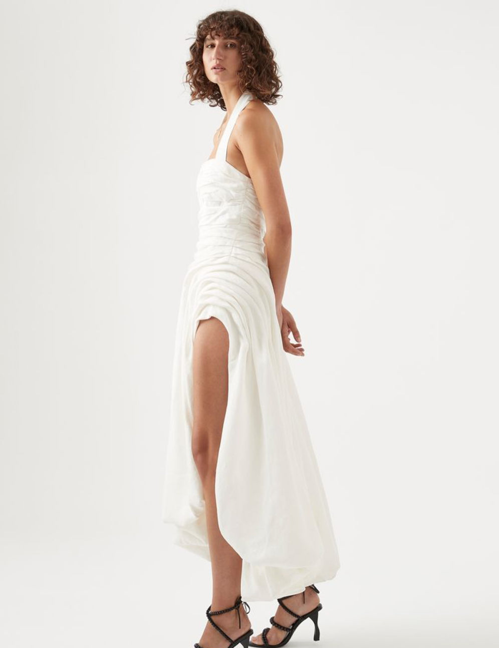 Elevate your elegance with the Mika Draped Split Maxi Dress in Ivory by Aje. Crafted from midweight ruched linen, this fully lined dress features a sophisticated asymmetrical hem that flows gracefully. The exposed back zipper adds a modern edge, while the gold-tone and faux pearl accents on the halterneck strap enhance its refined charm. Perfect for making a timeless statement at any upscale event.