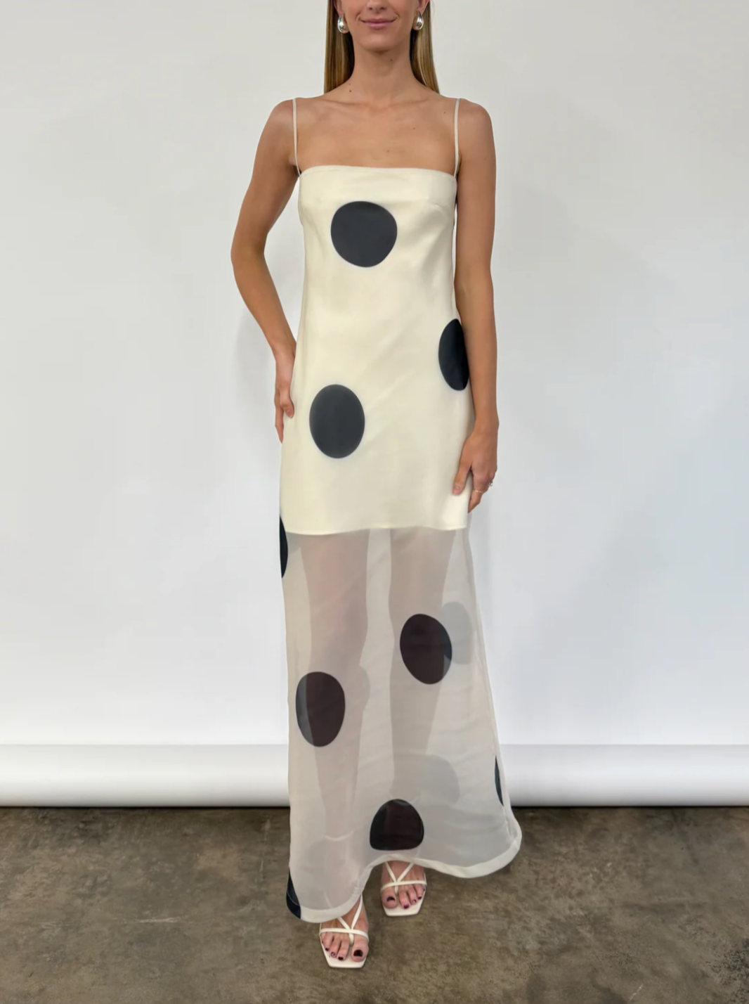 The Mila Maxi Dress in Ivory Polka by Nicole features sheer organza adorned with striking polka dots, shaping a sleek column silhouette. Its half-lined design and elasticated back ensure comfort and adaptability, while the option to wear it with or without straps provides versatile styling choices perfect for refined occasions.