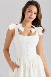 The Lillia Midi Dress exemplifies refined elegance with its expertly crafted stretch cotton fabric that contours the body comfortably. Its structured bodice features fabric-covered buttons along the front, designed to flatter your silhouette. Flowing from the hips, the skirt offers a delicate volume enhanced by a soft tulle lining and a lace-trimmed hem, creating a graceful and sophisticated look with every movement.