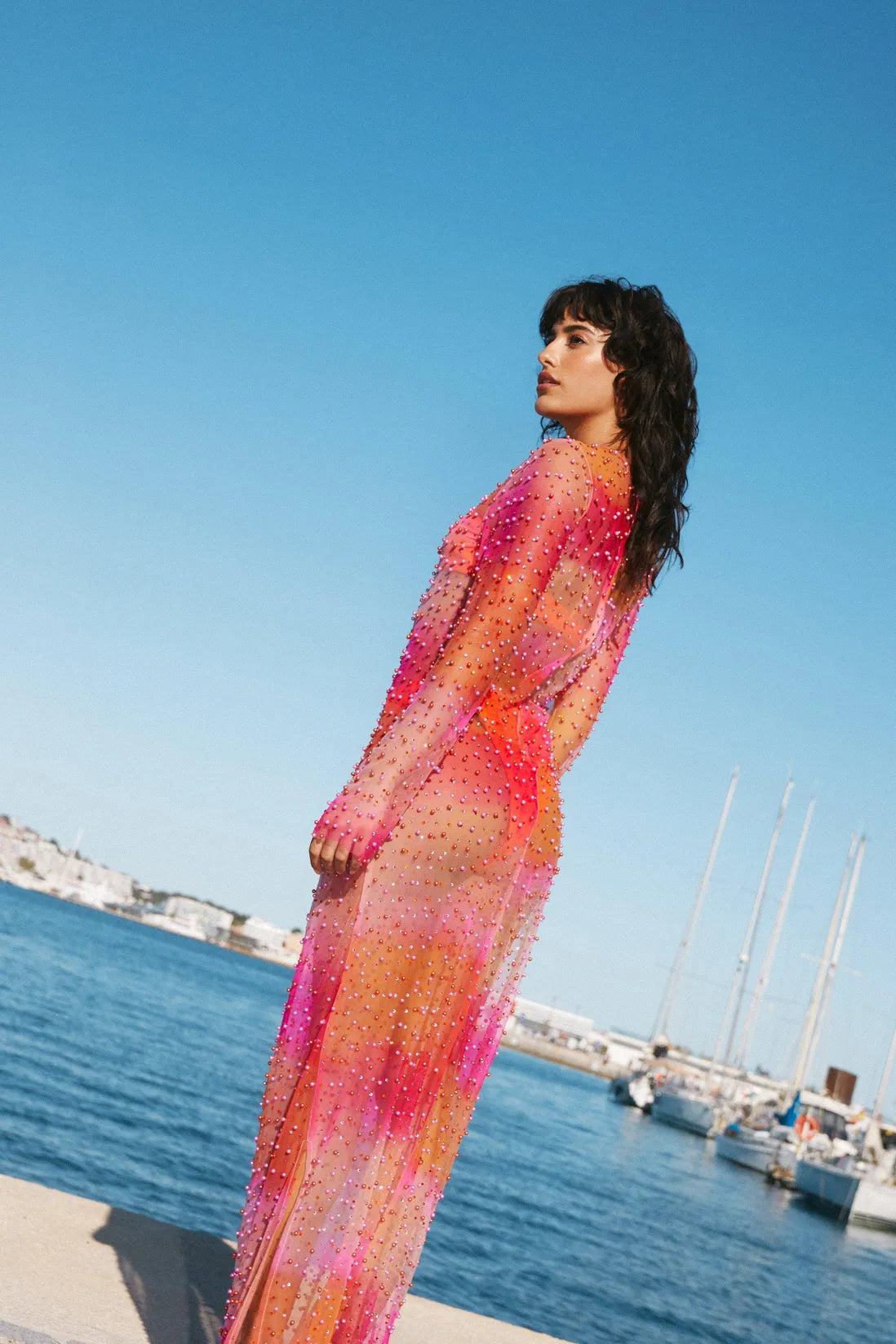 This Embellished Ombre Maxi Dress features premium mesh fabric adorned with sparkling pearls and diamante details for a striking, sheer look. Its gradient ombre colorway adds a modern edge, while the lightweight design ensures comfort. Perfectly styled over hotpants and a bandeau top with sandals, it transitions effortlessly from beach resort days to poolside evenings, blending elegance with playful sophistication.