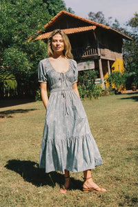 The Brynne Dress in the seasonal Pansy Blues print by Christy Dawn combines delicate femininity with adjustable comfort. It features a low scoop neckline complemented by a drawstring tie at both the neck and waist, allowing a custom fit that enhances your silhouette. Elasticated seams ensure ease of movement, making this dress as practical as it is stylish for versatile wear throughout the season.