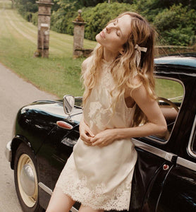 The Valeria Lace Dress in Candlelight combines buttery silk satin with refined 90s elegance. This sleeveless shift dress showcases a straight cut and a high neckline, offering a timeless silhouette. Its delicate lace details add a touch of playfulness, making it perfect for sophisticated occasions where subtle charm meets classic style.