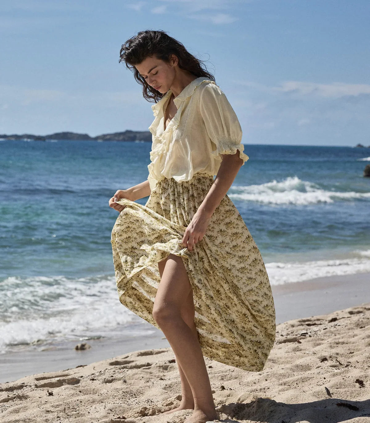 The DOEN Henri Top in Creme Citron exemplifies timeless elegance through its thoughtfully crafted design. Constructed from sumptuous organic cotton voile, this Edwardian-inspired piece features a striking plunging V-neckline complemented by delicate short puffed sleeves. Cascading lace-trimmed ruffles and refined pintucks create dimensional texture, while concealed starburst buttons at the center front provide subtle sophistication. 