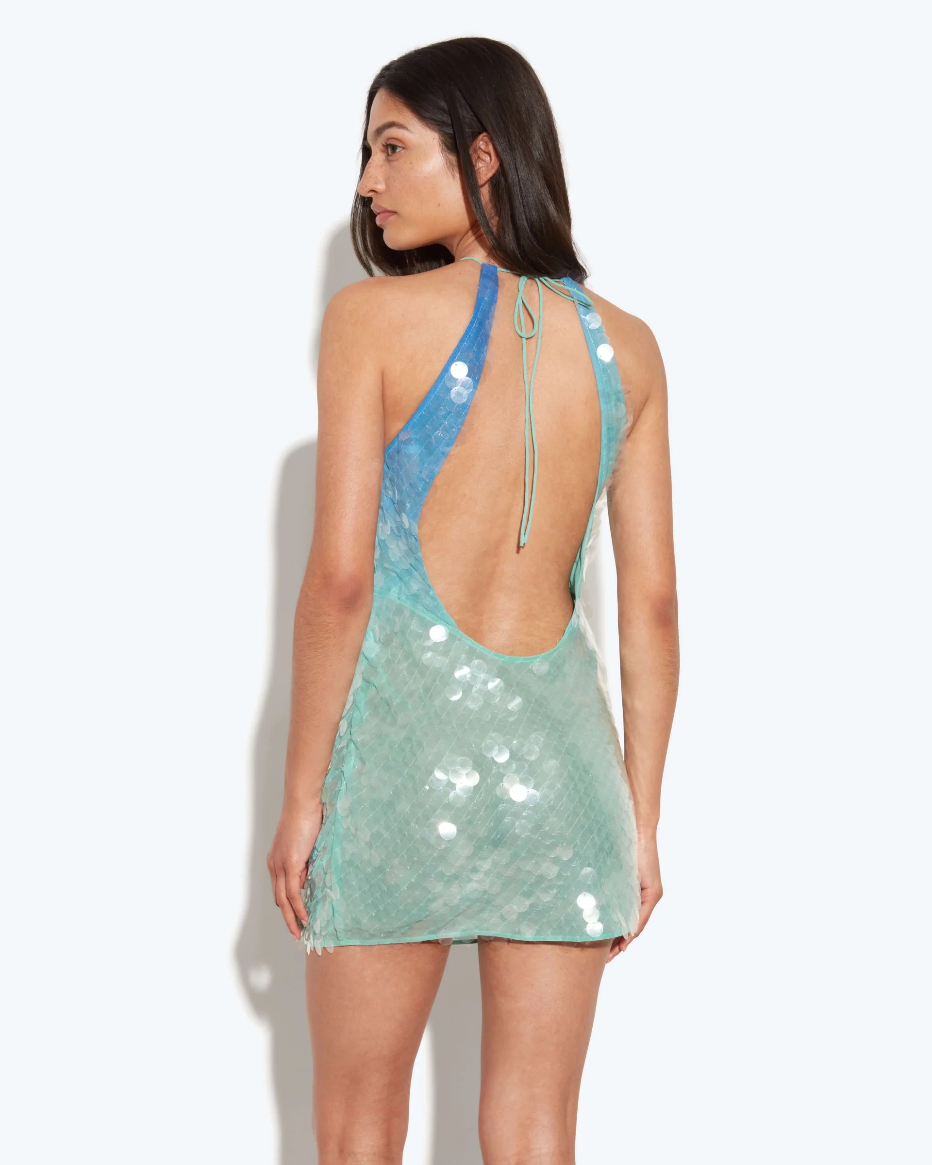 The Kiki Mini Dress dazzles with a molten sequin design that shifts in an ombré gradient from blue to green, capturing light with every movement. Its slinky silhouette is ideal for summer evenings, enhanced by a daring plunge back and an extreme cowl neckline that together create a strikingly sensual appeal. Perfect for making a bold statement at any night event.