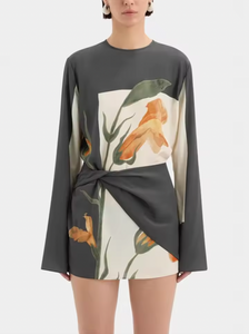 The Constance Twist Mini Dress is made from delicate silk crepe adorned with artistic floral prints and bold borders. This dress offers a relaxed silhouette, showcasing long sleeves with gentle flares and a distinctive contrasting overlay accented by a twisted detail at the waist.