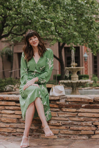 Show off your playful side in the Violette Midi Dress! This stunning lightweight silk dress features a white floral print on a vibrant green background. With 3/4 length sleeves and a comfortable wrap style, you can adjust the waist with the string tie closure. Embrace your love for summer in this unique and stylish dress!