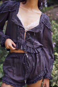 Experience timeless elegance with the Florence Set in Black, designed for both comfort and style. The structured bed jacket features front tie closures, delicate pleated piecing, and banded trumpet sleeves accented by intricate embroidery and ruffle trim. Coordinating shorts offer a drawstring waist for a customizable fit, complemented by ruffle details, pleated patterns, and embroidered accents with a graceful curved hem. Perfect for lounging with refined sophistication.