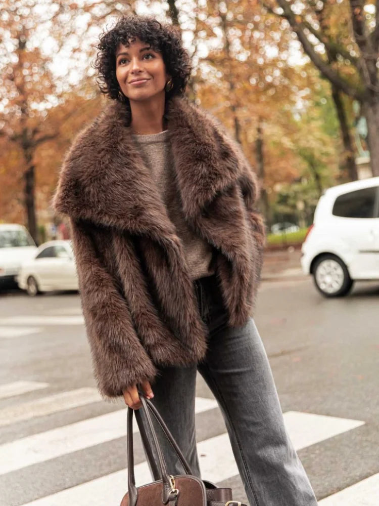 This short faux fur coat combines sophisticated style with practical details. Designed with a classic lapel collar and long sleeves, it offers warmth and elegance. Side pockets add convenience, while the tonal lining ensures a smooth fit. The front fastening with metal hooks provides secure closure and a sleek finish, making it an ideal choice for refined winter wear.