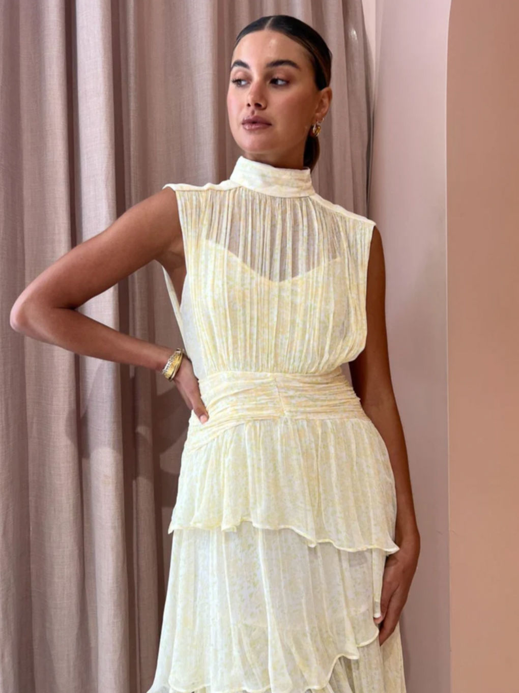 Introducing the Gina Sleeveless Ruched Midi Dress in Limoncello - a must-have for any special occasion. Crafted from semi-sheer chiffon, this dress boasts a high neck and adjustable rouleau straps for a perfect fit. With its fitted waist and asymmetrical tiered skirt, this dress exudes elegance and style. Perfect for formal events and celebrations.