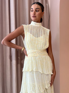 Introducing the Gina Sleeveless Ruched Midi Dress in Limoncello - a must-have for any special occasion. Crafted from semi-sheer chiffon, this dress boasts a high neck and adjustable rouleau straps for a perfect fit. With its fitted waist and asymmetrical tiered skirt, this dress exudes elegance and style. Perfect for formal events and celebrations.