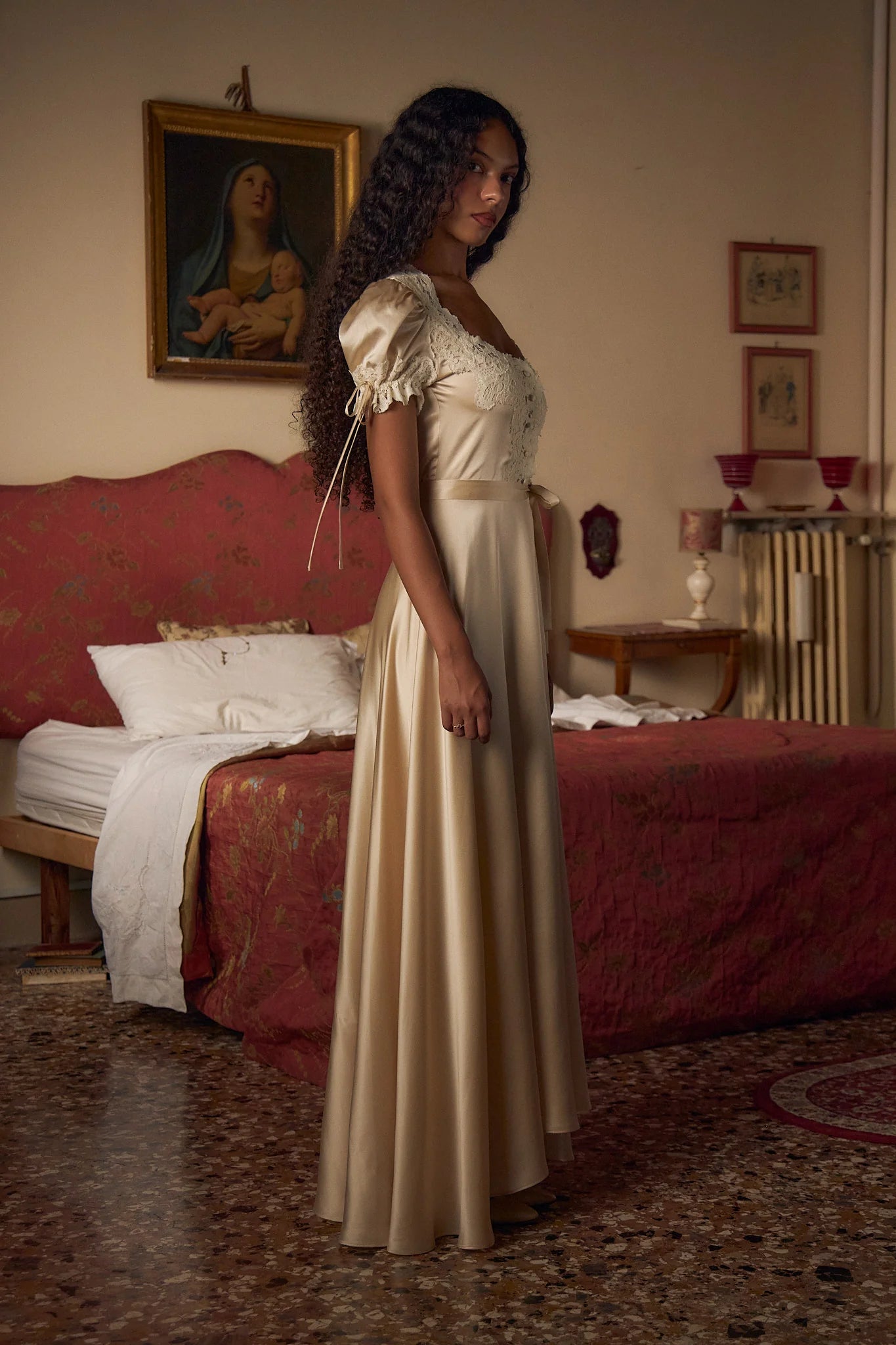 Crafted from luxurious silk charmeuse, the Unwrap Me Gown in Crème features delicate lace trim along the neckline and sleeves, enhancing its refined silhouette. Lace-covered buttons with hidden snaps offer elegant closure at the center front, while a matching silk charmeuse belt with chain stitch loops and snaps defines the waist. An adjustable slit secured by hook and thread loops adds both comfort and sophistication, making this gown a masterful blend of exquisite detail and expert tailoring.