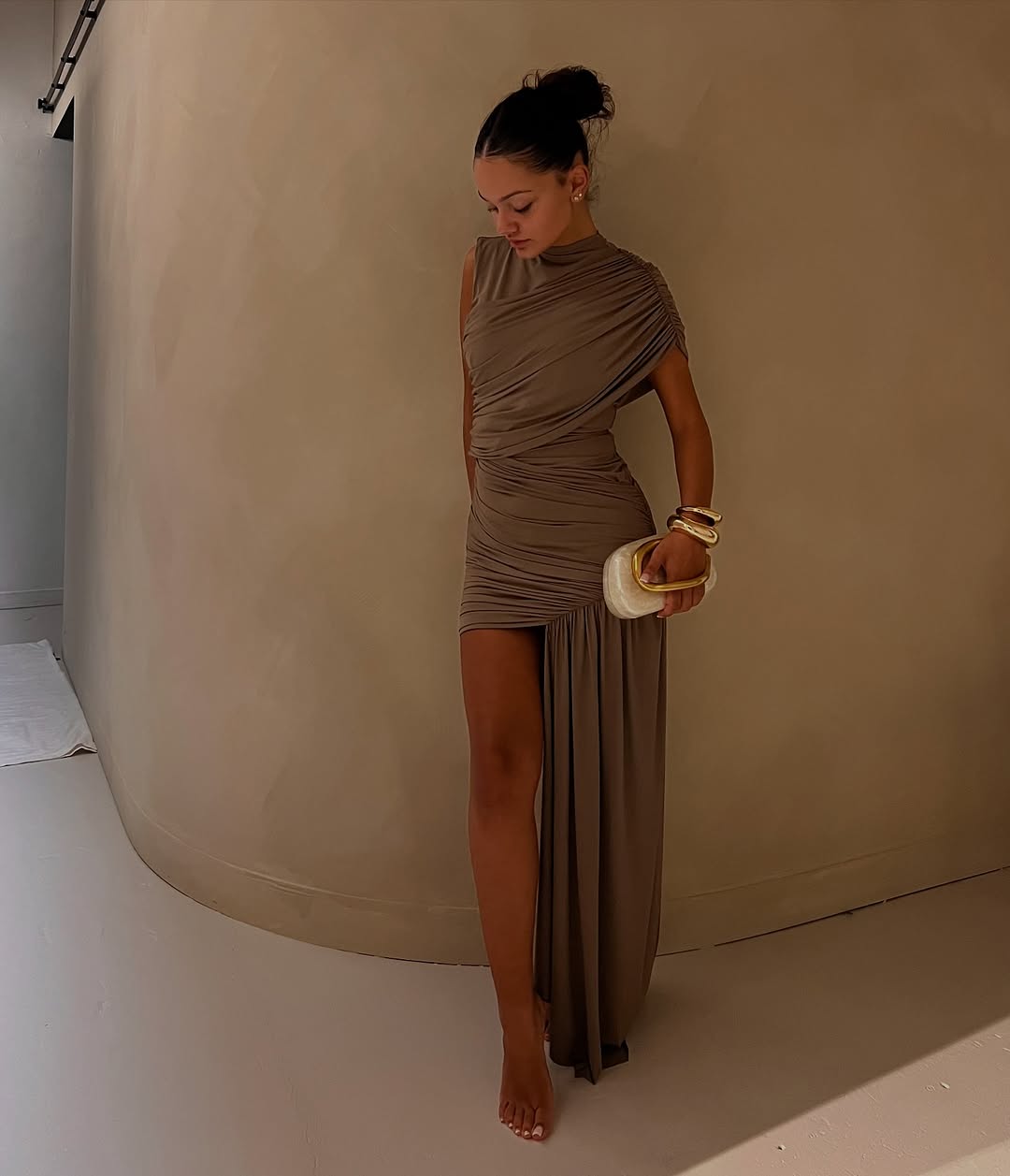 The Ravenna Dress in taupe features an asymmetrical high-low hemline and subtle ruching that accentuates a form-fitting silhouette. Sleeveless and true to size, it elegantly sculpts your shape for special occasions. Its refined taupe hue complements metallic accessories and classic pumps, offering a sophisticated and confident ensemble.