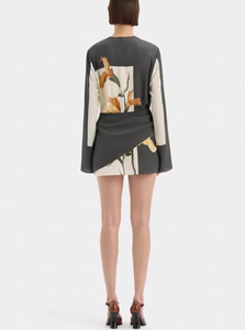 The Constance Twist Mini Dress is made from delicate silk crepe adorned with artistic floral prints and bold borders. This dress offers a relaxed silhouette, showcasing long sleeves with gentle flares and a distinctive contrasting overlay accented by a twisted detail at the waist.
