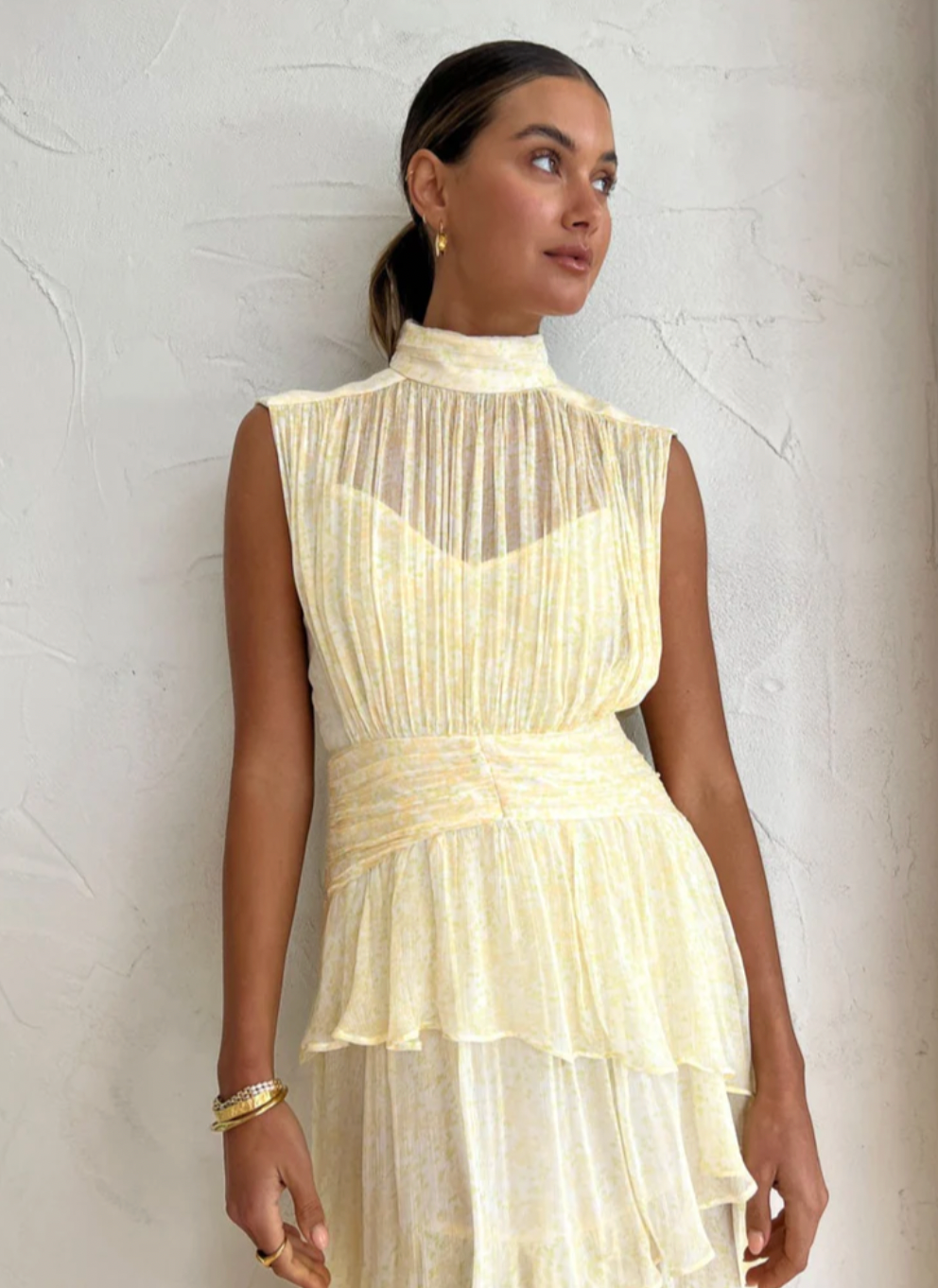 Introducing the Gina Sleeveless Ruched Midi Dress in Limoncello - a must-have for any special occasion. Crafted from semi-sheer chiffon, this dress boasts a high neck and adjustable rouleau straps for a perfect fit. With its fitted waist and asymmetrical tiered skirt, this dress exudes elegance and style. Perfect for formal events and celebrations.