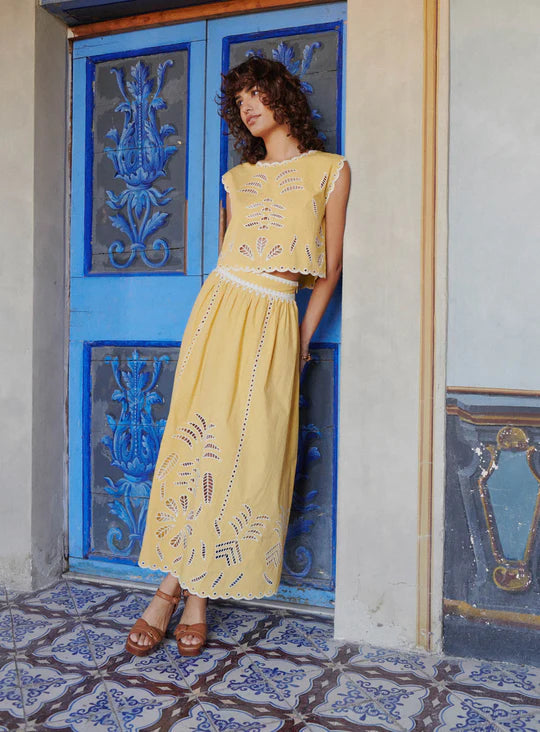 The Tiffany Set combines a vibrant skirt and top, expertly crafted to elevate your seasonal wardrobe. The skirt features intricate openwork patterns and a scalloped hem, enhanced with modernized iconic embroidery using inlaid guipure, adding refined elegance. The top complements with its sunny tone and delicate embroidery, versatile enough for pairing with high-waisted jeans or the matching skirt for a coordinated, feminine ensemble. 