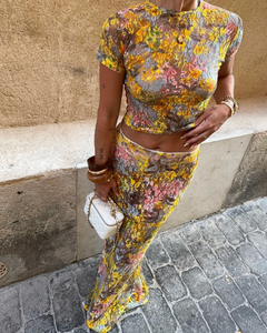 This elegant set features a multi-floral maxi skirt with a form-fitting silhouette that sits mid to low waist, crafted from luxurious stretchy lace for comfort and style. Complemented by a coordinating semi-sheer floral baby t-shirt with cap sleeves and a cropped shape, both pieces showcase a bright summer palette and timeless design, perfect for a sophisticated seasonal look.