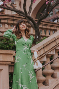 Show off your playful side in the Violette Midi Dress! This stunning lightweight silk dress features a white floral print on a vibrant green background. With 3/4 length sleeves and a comfortable wrap style, you can adjust the waist with the string tie closure. Embrace your love for summer in this unique and stylish dress!