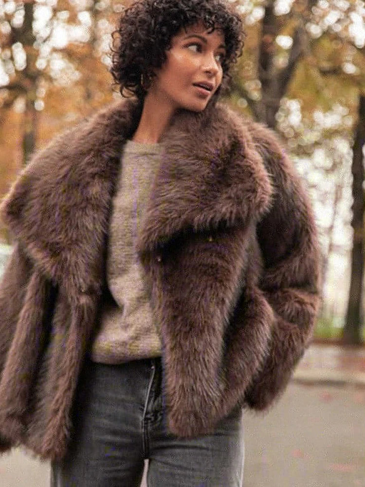 This short faux fur coat combines sophisticated style with practical details. Designed with a classic lapel collar and long sleeves, it offers warmth and elegance. Side pockets add convenience, while the tonal lining ensures a smooth fit. The front fastening with metal hooks provides secure closure and a sleek finish, making it an ideal choice for refined winter wear.
