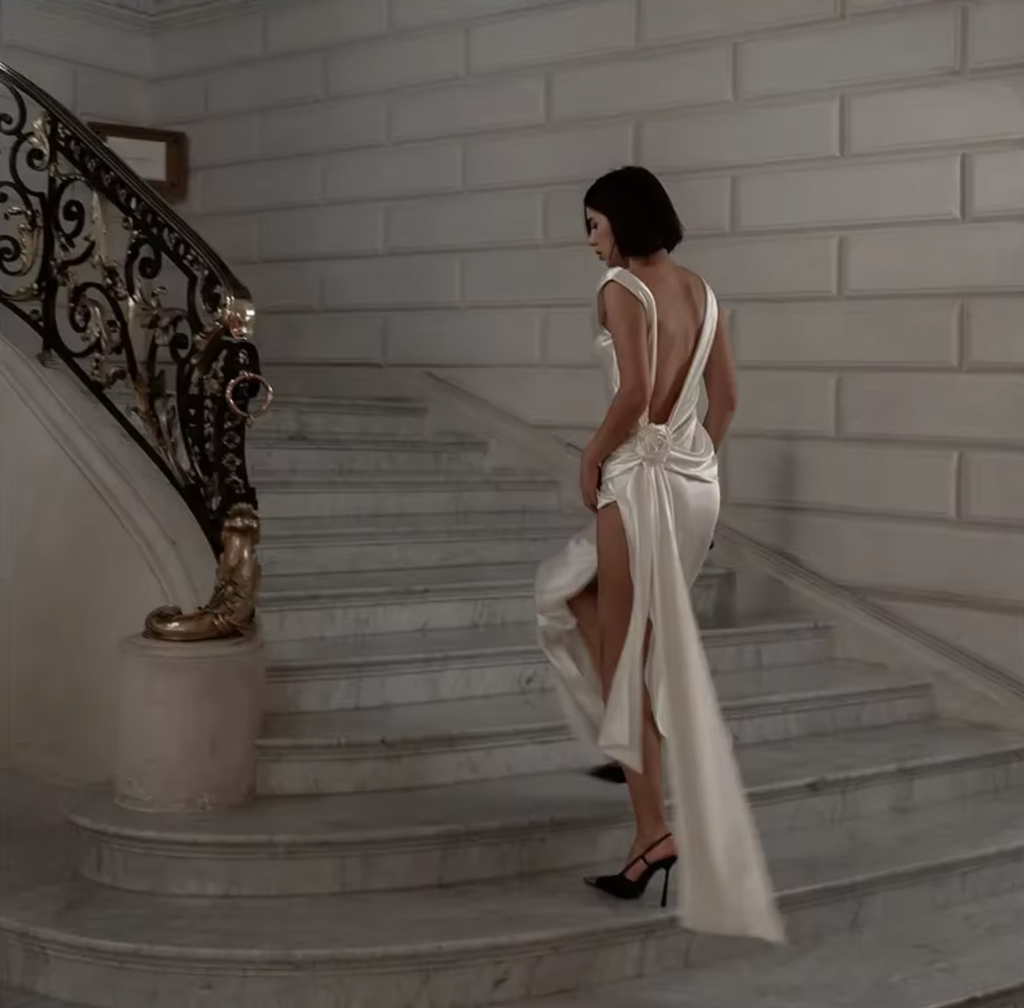 Indulge in luxury with the Darling Gown by DATT. Made from sumptuous silk, this gown exudes elegance. The back split adds a touch of allure while the intricate 3D rose embellishment elevates the design to a work of art. Perfect for those seeking a sophisticated and exclusive piece for their wardrobe.