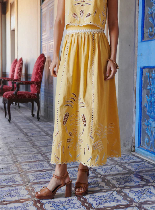 The Tiffany Set combines a vibrant skirt and top, expertly crafted to elevate your seasonal wardrobe. The skirt features intricate openwork patterns and a scalloped hem, enhanced with modernized iconic embroidery using inlaid guipure, adding refined elegance. The top complements with its sunny tone and delicate embroidery, versatile enough for pairing with high-waisted jeans or the matching skirt for a coordinated, feminine ensemble. 