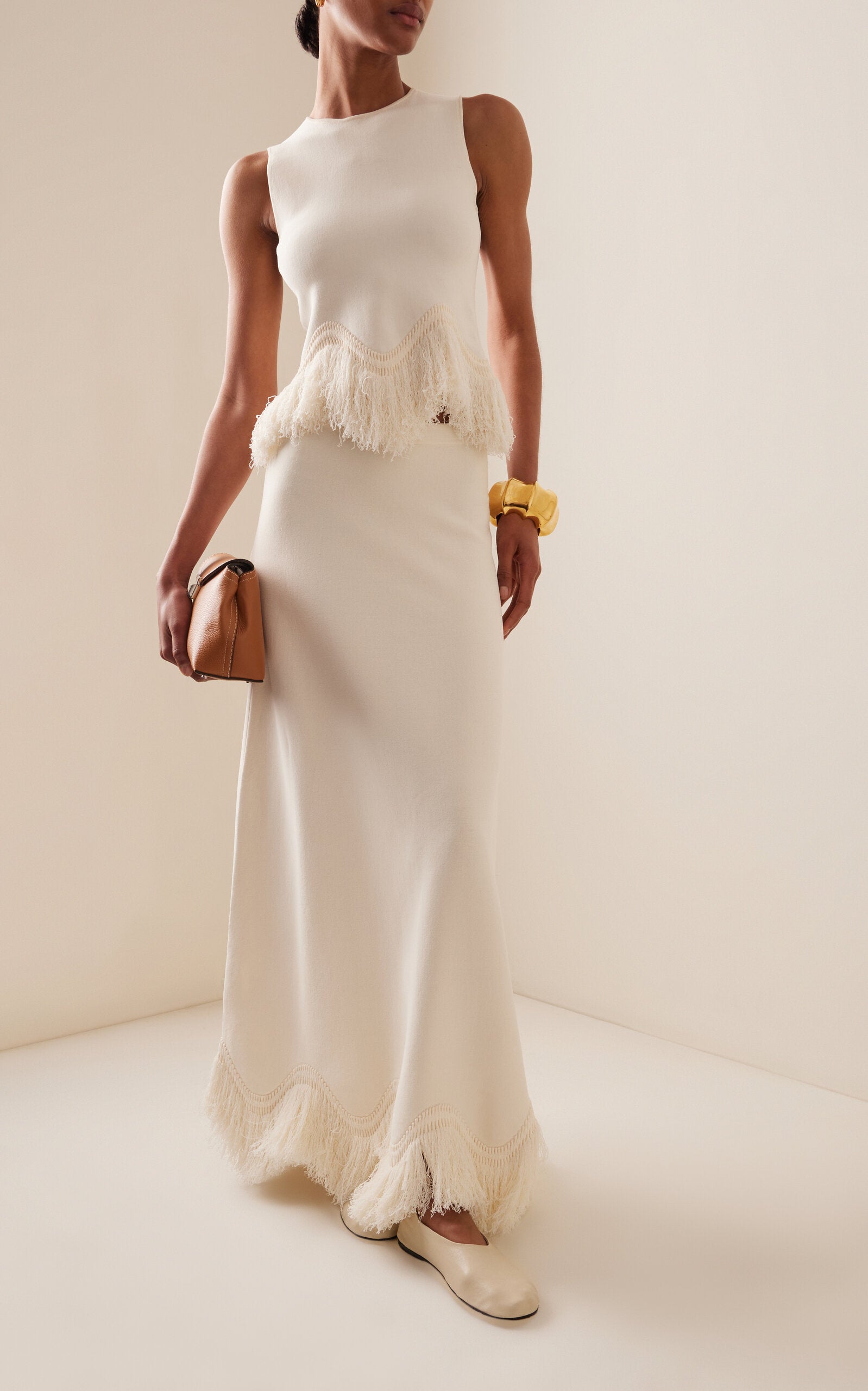 The 'Paulina' skirt offers a graceful A-line shape that gently widens toward its distinctive zig-zag fringe-trimmed hem. Complete the look by pairing it with the coordinating 'Koa' top, which boasts a sleek, sleeveless design accented by a matching zig-zag fringe detail at the hem.