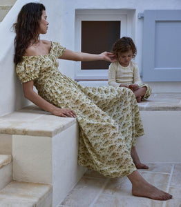 Crafted from soft, lightweight organic cotton voile, the Ashlynn Dress in Citron Rosier Floral by Doen blends Victorian elegance with modern comfort. Featuring short puffed sleeves, a scoop neckline with a functional center tie, and delicate ruffled cuffs, this dress exudes vintage charm. The smocked bodice ensures a flattering fit, complemented by an adjustable waist tie, while the full, ankle-grazing skirt offers graceful movement. Ideal for those seeking refined style with breathable, sustainable fabric.