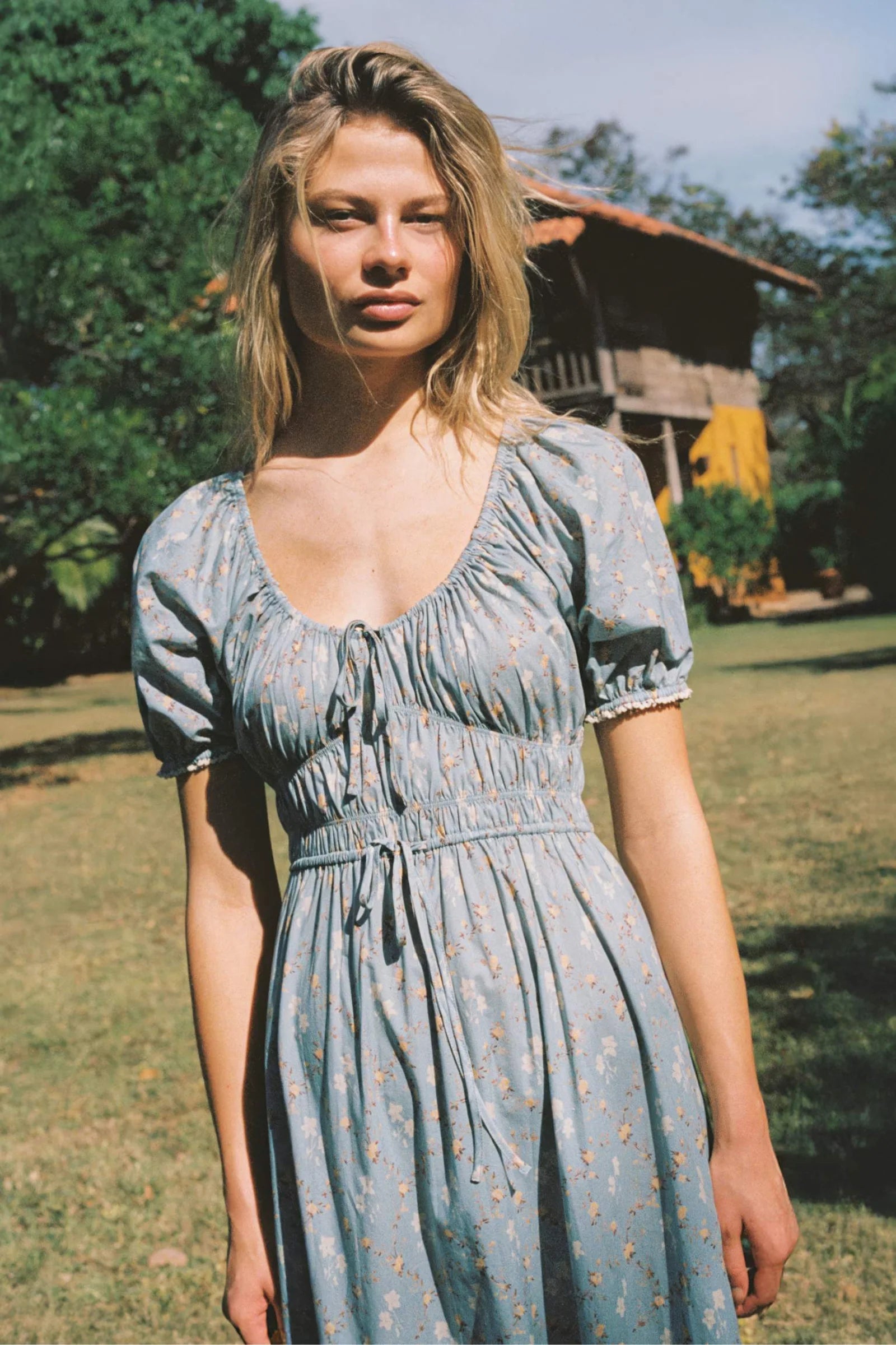 The Brynne Dress in the seasonal Pansy Blues print by Christy Dawn combines delicate femininity with adjustable comfort. It features a low scoop neckline complemented by a drawstring tie at both the neck and waist, allowing a custom fit that enhances your silhouette. Elasticated seams ensure ease of movement, making this dress as practical as it is stylish for versatile wear throughout the season.